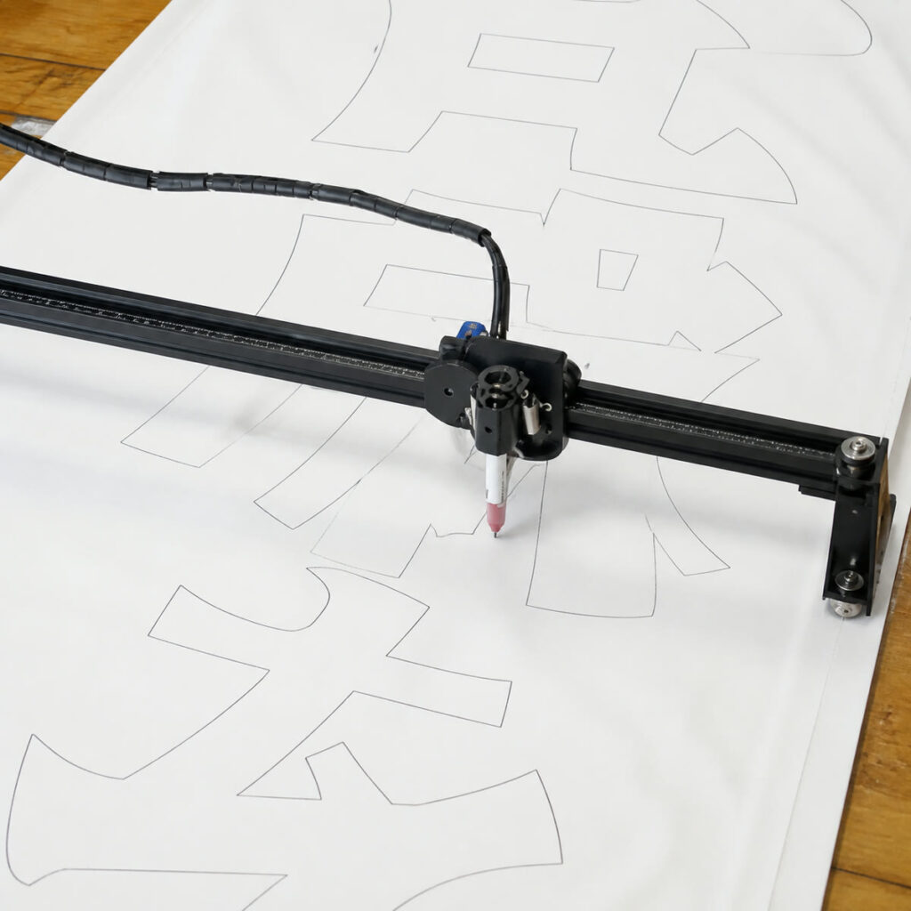自作ペンプロッターが横断幕用の文字輪郭を描いている様子